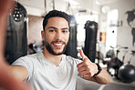 Portrait of one confident young hispanic man taking selfies and gesturing thumbs up while exercising in a gym. Happy mixed race instructor looking motivated and ready for a good training workout in a fitness centre