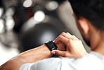 Closeup of one mixed race man checking his digital wristwatch with blank display screen while training in a gym. Guy from above wearing fitness tracker on arm to monitor progress, heart rate and calories burned during exercise in a fitness centre