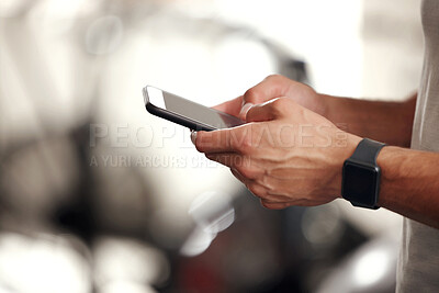 Closeup of one fit mixed race man using a cellphone while taking a break from exercise in a gym. Hands of a guy texting and browsing fitness apps online while checking social media during a rest from training workout