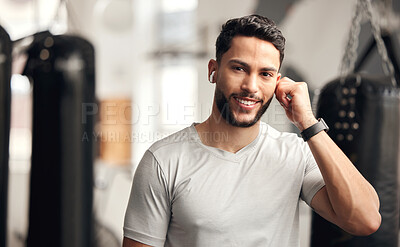 Portrait of one confident young hispanic man listening to music with wireless bluetooth earphones to stay motivated while exercising in a gym. Happy fit mixed race guy getting ready for training workout with his favourite songs on a playlist