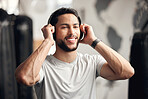 One confident young hispanic man listening to music with wireless bluetooth headphones to stay motivated while exercising in a gym. Happy fit mixed race guy getting ready for training workout with his favourite songs on a playlist in a fitness centre