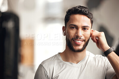 Buy stock photo Portrait of one confident young hispanic man listening to music with wireless bluetooth earphones to stay motivated while exercising in a gym. Happy fit mixed race guy getting ready for training workout with his favourite songs on a playlist