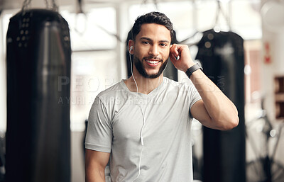 Portrait of one confident young hispanic man listening to music with earphones to stay motivated while exercising in a gym. Happy fit mixed race guy getting ready for training workout with his favourite songs on a playlist in a fitness centre