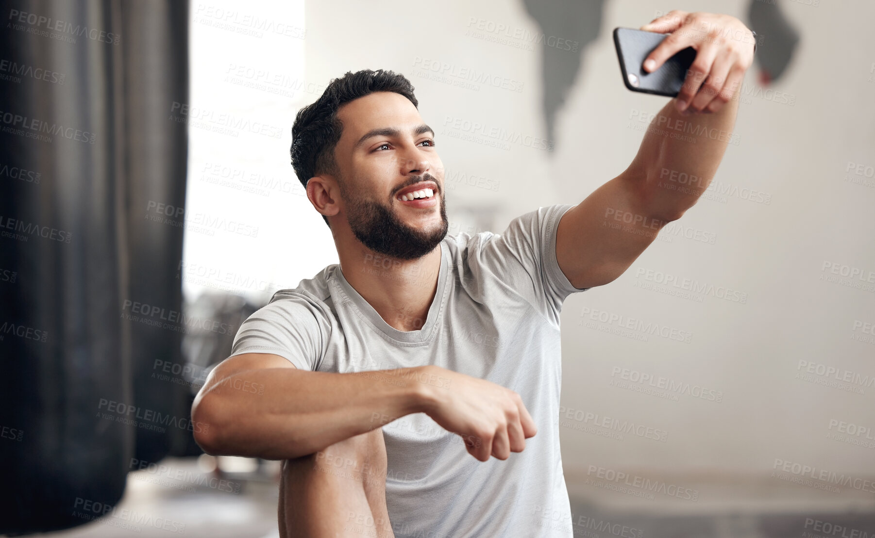 Buy stock photo One fit young hispanic man using a cellphone to take selfies while on a break from training in a gym. Happy mixed race guy making video call and taking photos for social media during a rest from workout