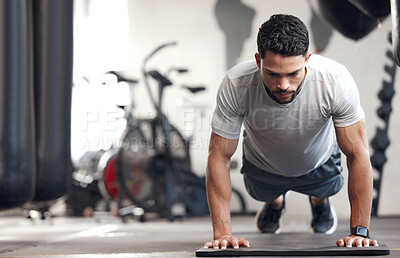 One fit young hispanic man doing bodyweight push up exercises while training in a gym. Muscular focused guy doing press ups and a plank hold to build muscle, enhance upper body, strengthen core and increase endurance during a training workout