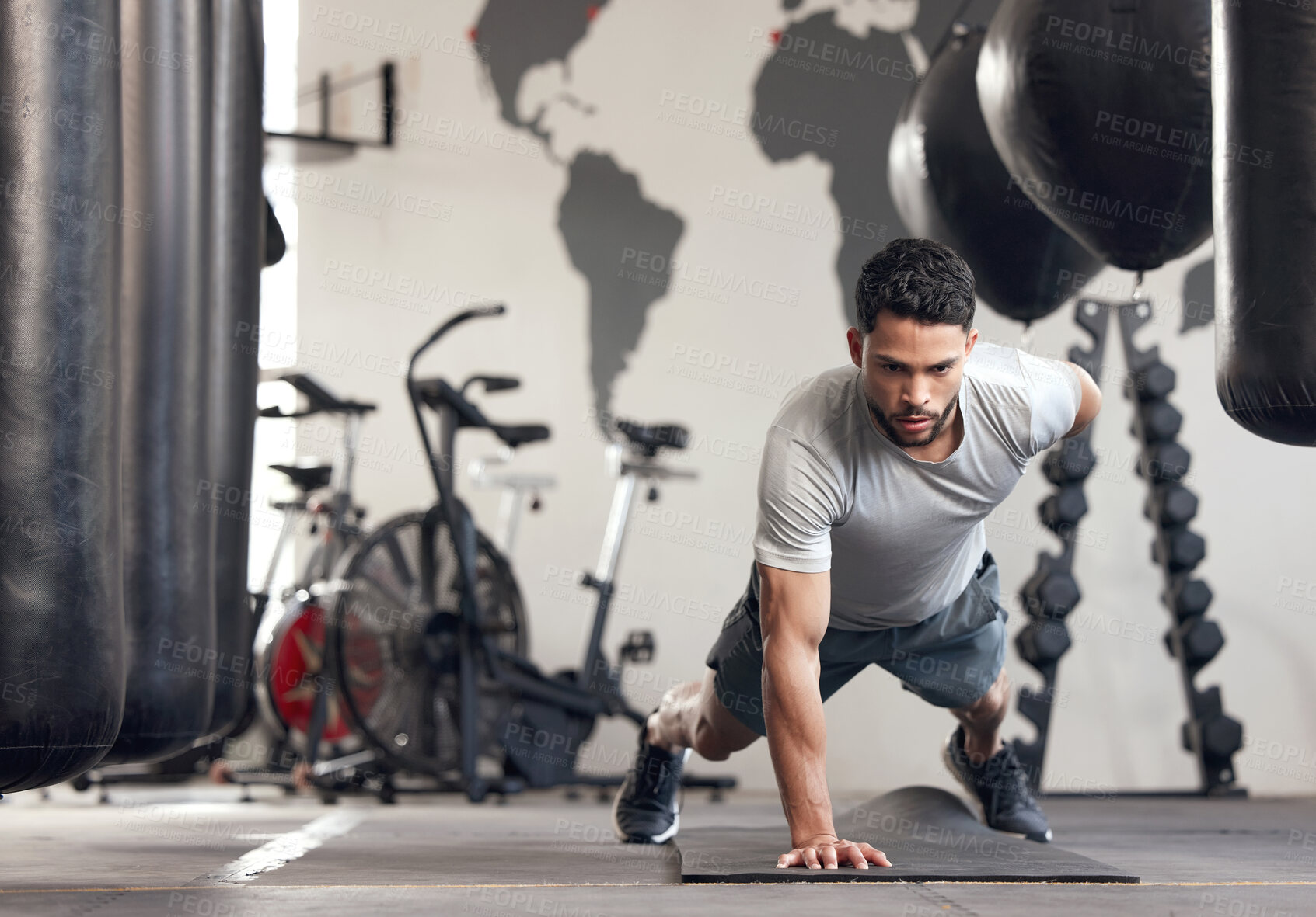 Buy stock photo Fit young hispanic man doing one arm bodyweight push up exercises while training in a gym. Muscular focused guy doing challenging press ups and a plank hold to build muscle, enhance upper body, strengthen core and increase endurance during a workout