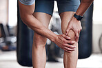 Closeup of one mixed race man holding his sore knee while exercising in a gym. Guy suffering with painful leg injury from fractured joint and inflamed muscles during workout. Struggling with stiff body cramps causing discomfort and strain