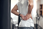 Closeup of one mixed race man holding his sore lower back while exercising in a gym. Guy suffering with painful spine injury from fractured joint and inflamed muscles during workout. Struggling with stiff body cramps causing discomfort and strain