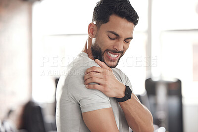 One young hispanic man holding his sore shoulder while exercising in a gym. Guy suffering with painful arm injury from fractured joint and inflamed muscles during workout. Struggling with stiff body cramps causing discomfort and strain