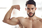 Portrait of one fit young hispanic man flexing his biceps to show big strong muscles from regular exercise in a gym. Serious bodybuilder with toned arms and sexy physique. Topless athlete proud of physical progress and powerful form