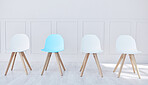 Four chairs lined up in an office waiting room. One blue chair and three white, waiting for potential job candidates to be seated, interviewed and potentially hired by human resources for a new career