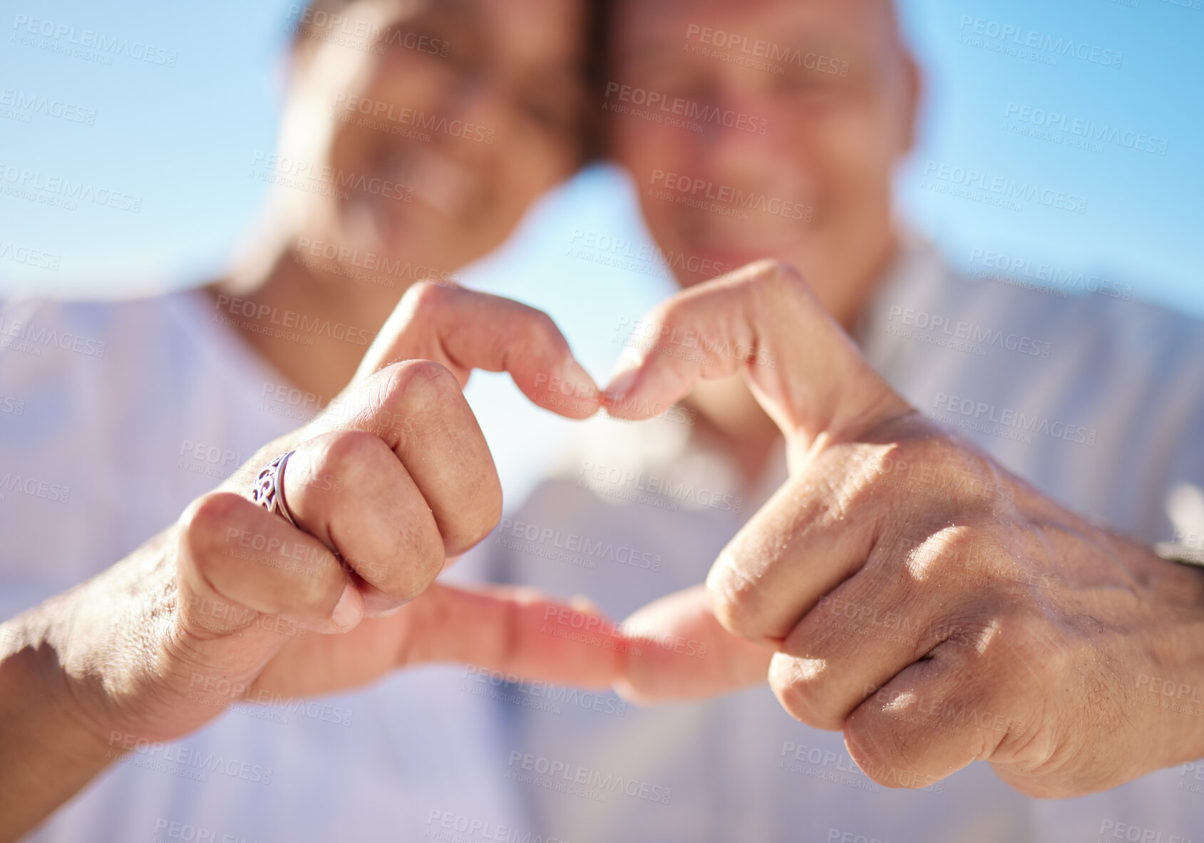 Buy stock photo Affectionate mature mixed race couple sharing an intimate moment on the beach. Senior husband and wife making a heart shape with their hands. They love spending time together by the sea at sunset