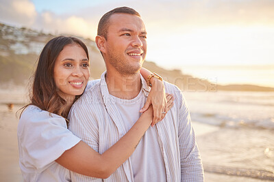 Affectionate young mixed race couple sharing an intimate moment on the beach. Happy husband and smiling wife enjoying a summer day by the sea. They love spending time together on the coast at sunset