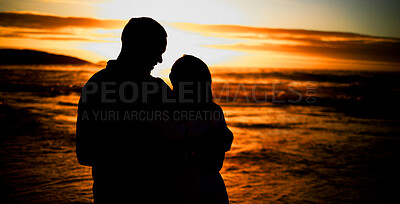 Silhouette affectionate young couple sharing an intimate moment on the beach. Backlit happy husband and wife enjoying a summer day by the sea. They love spending time together on the coast at sunset