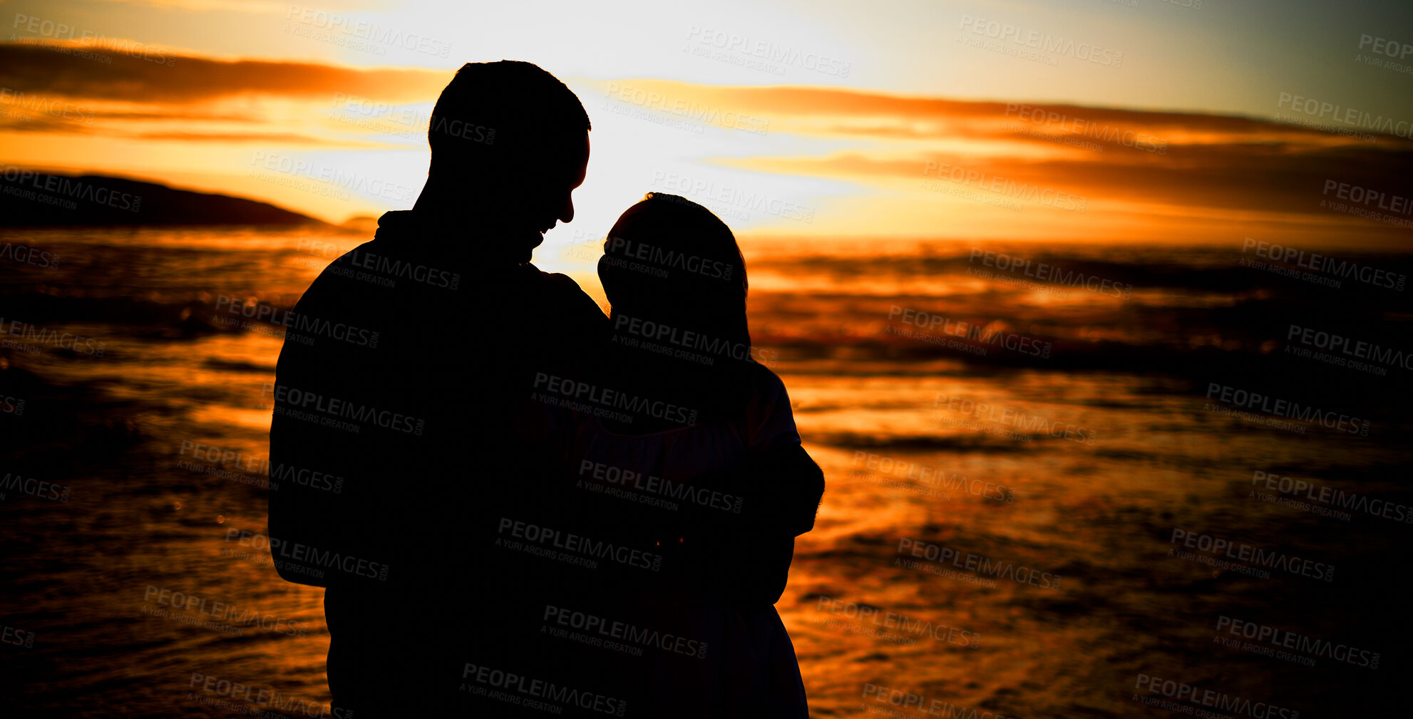 Buy stock photo Silhouette affectionate young couple sharing an intimate moment on the beach. Backlit happy husband and wife enjoying a summer day by the sea. They love spending time together on the coast at sunset