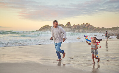 Cute little girl and her mixed race dad flying a kite on the beach. Adorable daughter and her handsome father running and playing in the sand next to the sea at sunset. Family bonding and happiness