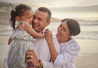 Buy stock photo Cute mixed race girl being held outside by her dad and grandmother in the sea at the beach. A young man and his mom holding his cute daughter while standing in the water on the coast at sunset