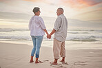 Rearview affectionate mature mixed race couple standing hand in hand on the beach. Senior husband and wife holding hands by the sea. They love spending time together on the coast in summer at sunset