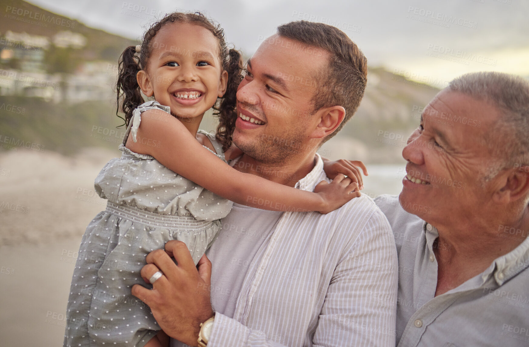 Buy stock photo Cute mixed race girl being held outside by her dad and grandfather in the sea at the beach. A young man and his dad holding his cute daughter while standing in the water on the coast at sunset