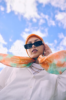 Buy stock photo Portrait, fashion or hijab with a saudi woman outdoor on a blue sky background in a scarf and sunglasses for style. Muslim, faith or religion with a trendy young arab person outside in modern clothes