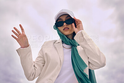 Buy stock photo Portrait, fashion or religion with a muslim woman on a cloudy sky background in a cap and scarf for modern style. Islam, faith or hijab with a trendy young arab person outside in contemporary clothes