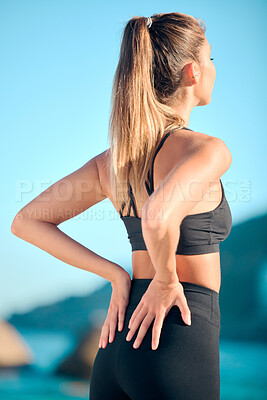 Rearview beautiful woman practising yoga exercise on the beach. Young female athlete suffering with back pain while working out outside. Struggling with cramp, soreness or stiffness of the muscle