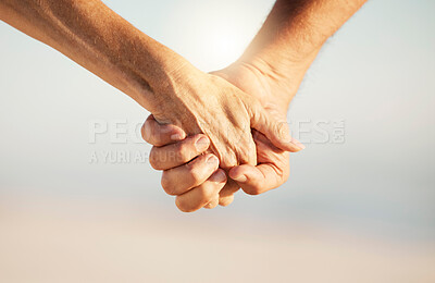 Closeup of senior couple holding hands on the beach. Mature couple holding hands by the ocean cropped. Hands of a married senior couple on holiday together. Mature couple holding hands on the beach