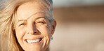Face of beautiful mature woman on the beach. Smiling senior woman enjoying a beach holiday. Closeup on face of happy senior woman by the ocean. Portrait of a happy woman enjoying a vacation by the sea