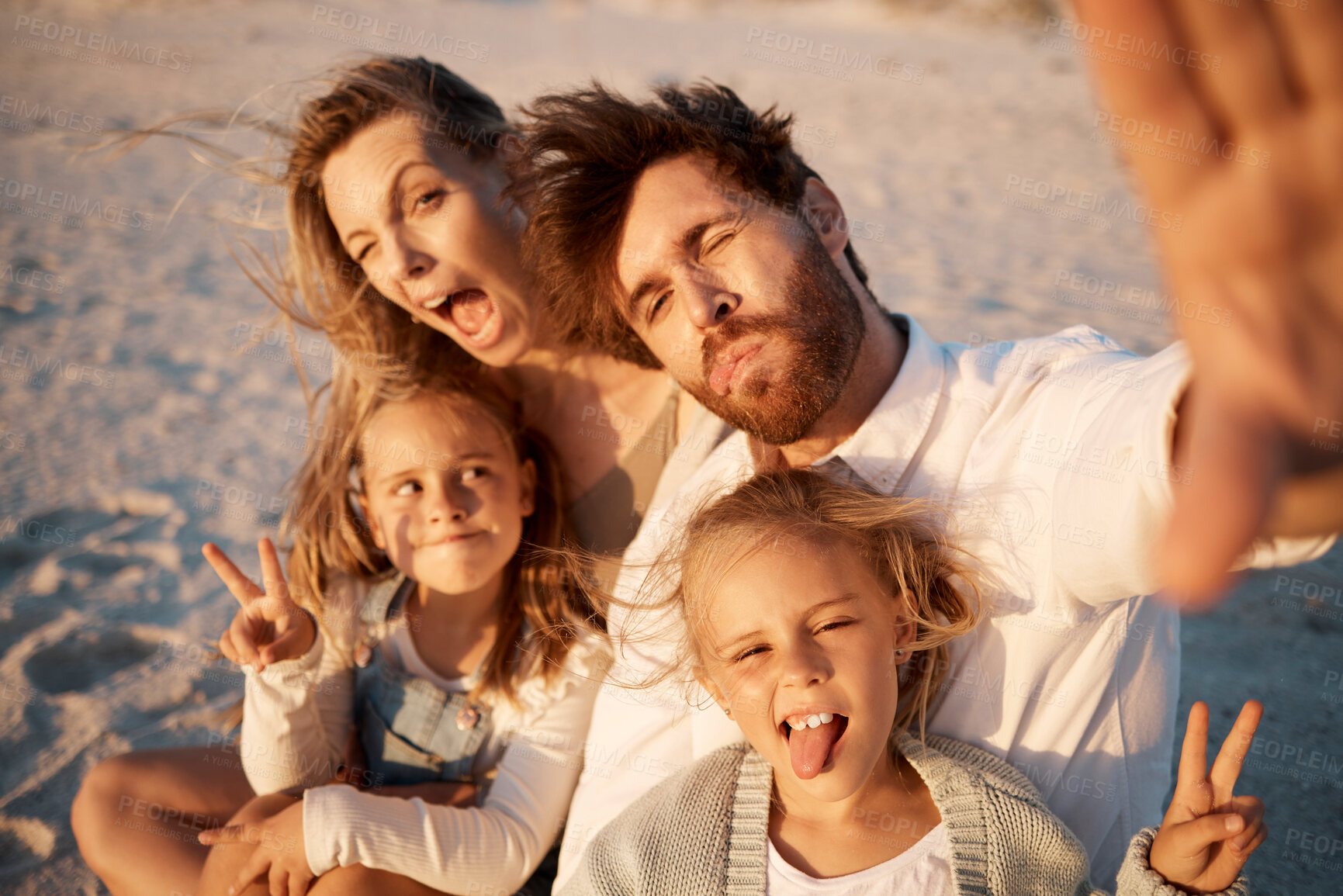 Buy stock photo Family having fun taking a selfie on the beach. carefree family making silly faces in a selfie. Happy father taking a photo with his family. Little girls having fun with their parents by the ocean