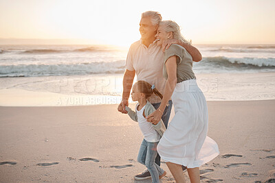 Buy stock photo Mature couple strolling on the beach together. Happy senior grandparents walking with their grandchild. Little girl bonding with her grandparents on holiday. Mature man hugging his wife on the beach