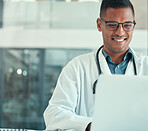 Medical doctor working on his laptop. Young doctor typing on his laptop in the hospital. Smiling doctor browsing the internet on his laptop. Young man using his computer in the clinic