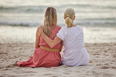 Rear view of a caucasian mother and daughter sitting on the sand at the beach together and bonding looking at the view