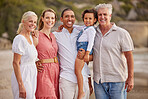 Portrait of a senior caucasian couple at the beach with their children and grandchild. Mixed race family relaxing on the beach having fun and bonding