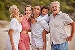 Portrait of a senior caucasian couple at the beach with their children and grandchild. Mixed race family relaxing on the beach having fun and bonding