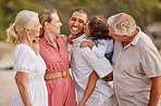Closeup of a senior caucasian couple at the beach with their children and grandchild. Mixed race family relaxing on the beach having fun and bonding