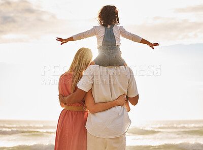 Rear view of mixed race family walking along the beach enjoying vacation. Adorable little sitting on her father\'s shoulders while enjoying family time by the beach with her two parents