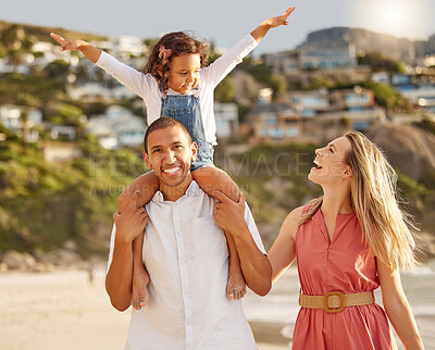 Happy mixed race family walking along the beach enjoying vacation. Adorable little sitting on her fathers shoulders while enjoying family time by the beach with her two parents