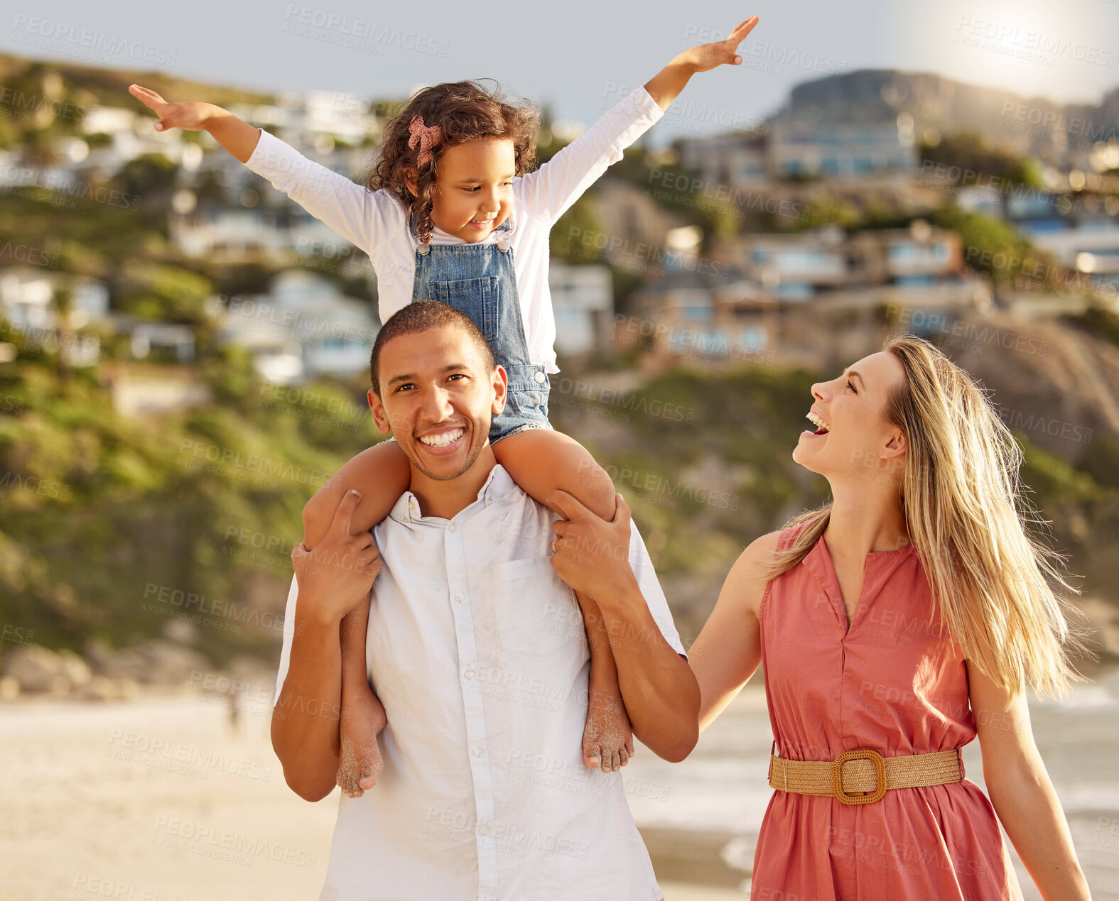 Buy stock photo Happy mixed race family walking along the beach enjoying vacation. Adorable little sitting on her fathers shoulders while enjoying family time by the beach with her two parents