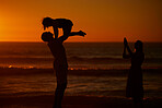 A young family silhouetted on the beach while playing together. Cheerful family with one child, two parents and daughter having fun during sunset at the beach