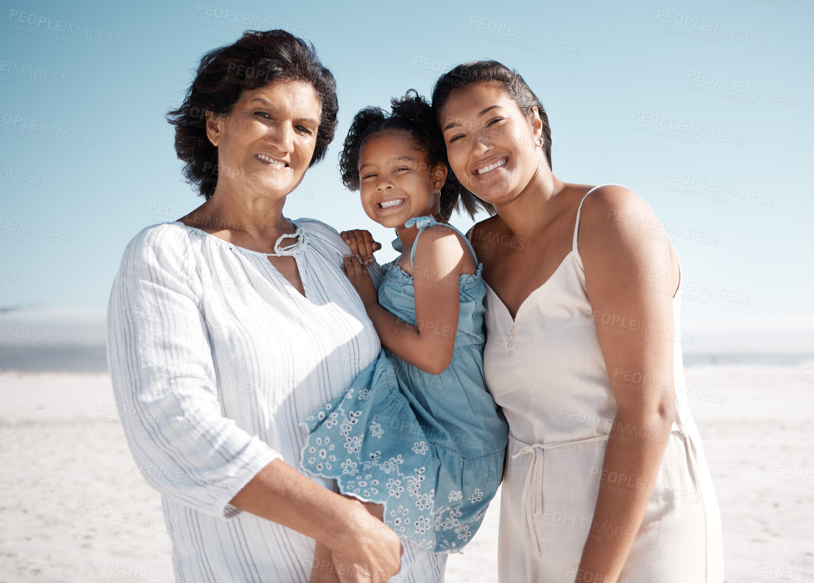 Buy stock photo Smiling mixed race family standing together on a beach. Happy hispanic grandmother bonding with granddaughter over a weekend. Adorable little girl enjoying free time with single mother and parent