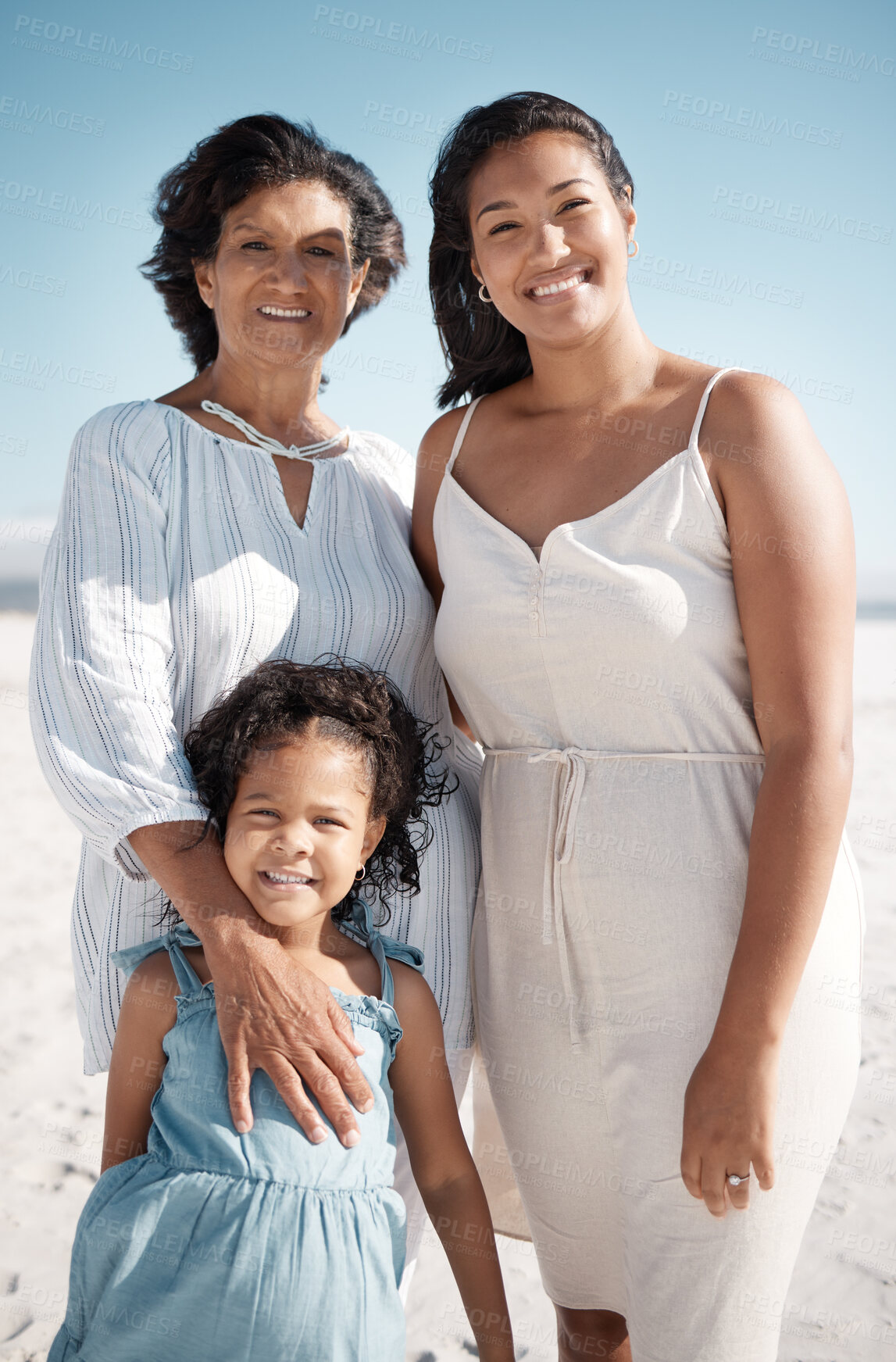 Buy stock photo Smiling mixed race family standing together on a beach. Happy hispanic grandmother bonding with granddaughter over a weekend. Adorable little girl enjoying free time with single mother and parent