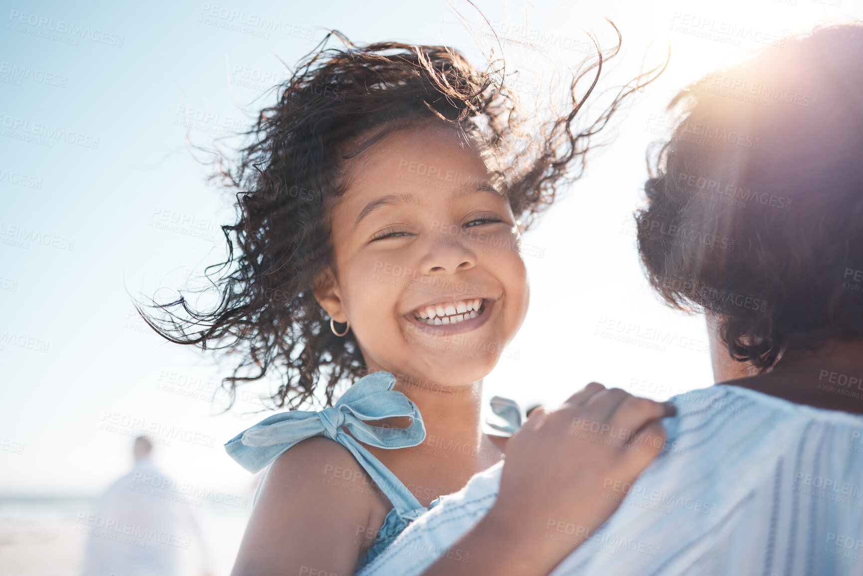 Buy stock photo Smiling mixed race little girl being carried by grandmother on beach. Happy hispanic granddaughter bonding with family over a weekend. Adorable little child enjoying free time and the wind in her hair