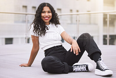 Beautiful mixed race fashion woman sitting outside in the city during the day. Young hispanic woman looking stylish and trendy, smiling and happy while outdoors in summer. Carefree and fashionable