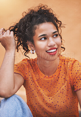 Closeup beautiful mixed race fashion woman looking thoughtful and smiling against an orange wall background in the city. Young hispanic woman looking stylish and trendy. Fashionable and carefree