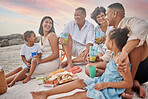 Closeup of a mixed race family having a picnic on the beach and smiling  while having some food with snacks. Happy family bonding on a day out at the beach