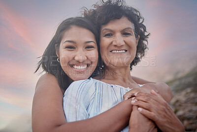 Buy stock photo Portrait of a young hispanic woman spending the day at the beach with her elderly mother. Mixed race female and her mother smiling at the beach and hugging each other