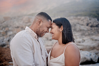 Buy stock photo Closeup of an young affectionate mixed race couple standing on the beach and smiling during sunset outdoors. Hispanic couple showing love and affection on a romantic date at the beach