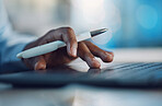 Closeup hands of african man holding a pen and working on a laptop. African american business man using computer while working late at night in his office. Putting in overtime after hours for success