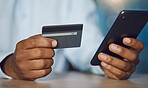 Closeup hands of african man using a phone while holding his credit card. African american business man shopping online while working late at night at his work. Putting in overtime after hours