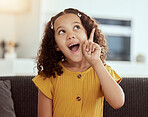 Adorable little mixed race child thinking at home. One small cute hispanic girl sitting alone on a sofa in a living room and coming up with an idea. Excited young kid with curly hair with a solution